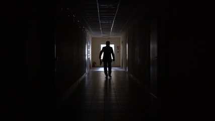 Fototapeta na wymiar Silhouette of a man runs through the dark corridor.