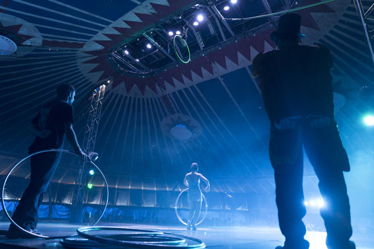 Circus peformer taking a bow with ringmaster and stage hand in foreground