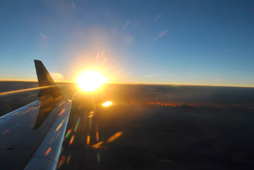 Airplane flying over the clouds with beautiful orange sunset beside its wing and some lens flares.