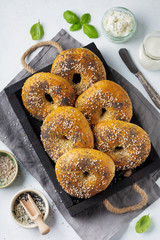 Variety fresh whole-grain bagels with poppy seeds, sesame seeds and ingredients for breakfast  on a light concrete or stone background. Selective focus. Top view. Copy space.