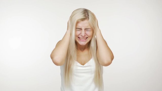 young blond woman getting hysterical shouting covering ears with hands  doesn't want to listen closing eyes tight on white background. Concept of emotions