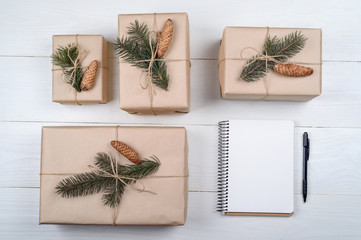 Top view of blank notebook on white wooden background with xmas decorations, copy space. Christmas background with notebook for wish list or to do list and gift boxes with fir tree branches. Flat lay
