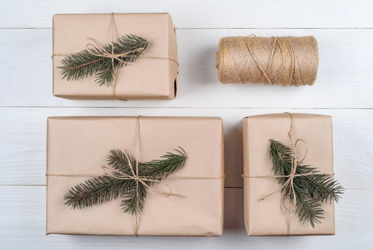 Christmas background with gift boxes wrapped in kraft paper with fir tree branches on white wooden background, free space. Holiday greeting card, copy space. Flat lay, top view