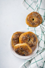 Bagels in a ceramic old bowl with a textile napkin on a light stone or concrete background. Selective focus. Top view. Copy space.