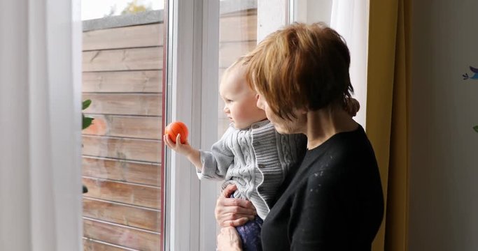 grandmother with grandchild looking through the window at home