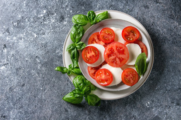 Italian caprese salad with sliced tomatoes, mozzarella cheese, basil. Served in ceramic over gray texture background. Top view with copy space. Restaurant menu