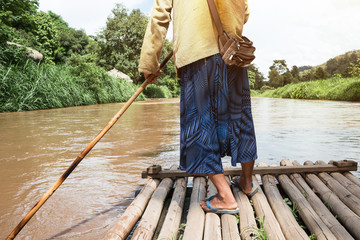 Man using pole to sail the bamboo raft in the river