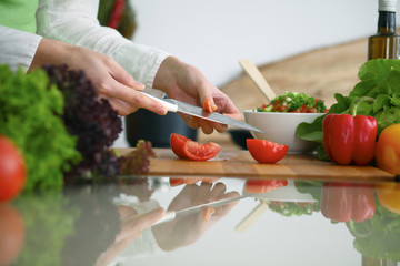 Closeup of human hands cooking vegetables salad in kitchen on the glass  table with reflection