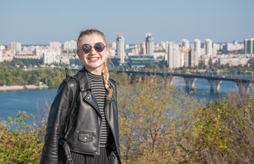 Beautiful blonde girl stands on the background of the city and smiles
