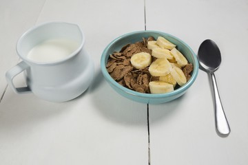 Wheat flakes and banana slice in bowl with milk jug