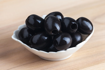 White bowl with black olives on wooden table