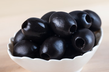 White bowl with black olives on wooden table