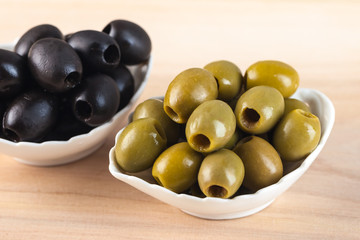 White bowlს with green and black olive on wooden table