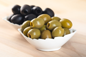 White bowl with green olives on wooden table