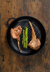 grilled lamb steak with asparagus in a frying pan on a wooden background