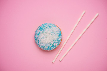 Blue donut with icing on pastel pink background with copyspace.