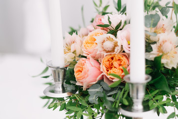Beautiful wedding floral decoration on a table in a restaurant. White tablecloths, bright room, candles, close-up shooting. The event, happiness, honeymooners. Soft bokeh white background