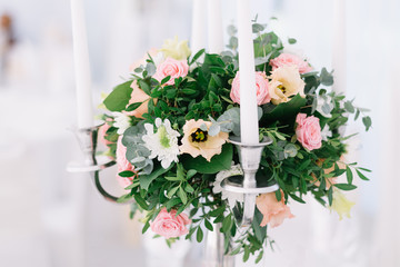 Beautiful wedding floral decoration on a table in a restaurant. White tablecloths, bright room, candles, close-up shooting. The event, happiness, honeymooners. Soft bokeh white background