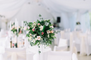 Beautiful wedding floral decoration on a table in a restaurant. White tablecloths, bright room, candles, close-up shooting. The event, happiness, honeymooners. Soft bokeh white background