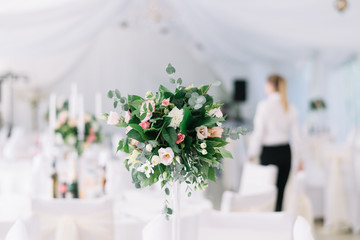 Beautiful wedding floral decoration on a table in a restaurant. White tablecloths, bright room, candles, close-up shooting. The event, happiness, honeymooners. Soft bokeh white background