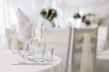 Table set for an event party or wedding reception on white tablecloth. White soft background with tables and flowers
