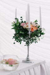 Beautiful wedding floral decoration on a table in a restaurant. White tablecloths, bright room, candles, close-up shooting. The event, happiness, honeymooners. Soft bokeh white background
