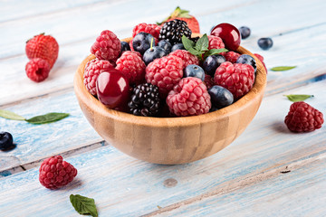 Fresh berries in a bowl on wooden background.