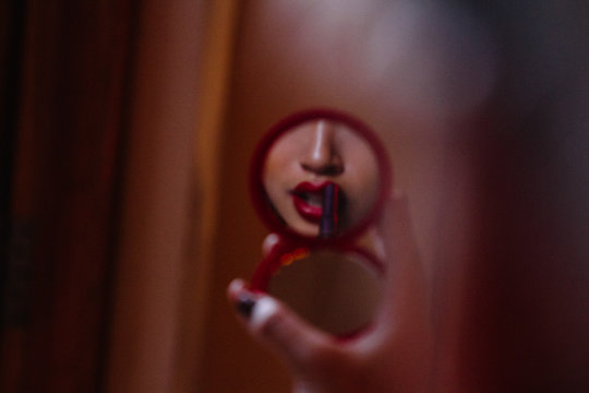 Young female asian model puts on makeup in mirror