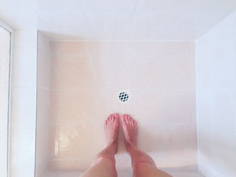 Looking down on woman's feet and legs in shower cubicle with running water