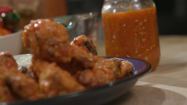 Chicken Wings rack Focus to Hot Sauce Angled. an angled close up shot of chicken wings on a plate racking focus to a container of hot sauce
