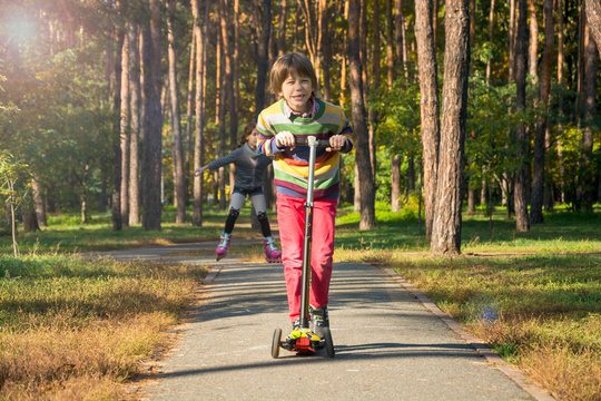 The boy is riding a scooter, followed by a girl with pigtails on rollers.