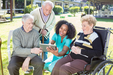 Fototapeta na wymiar Three active elderly people outdoor reading tablet with african nurse