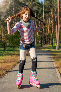Redhead girl with pigtails skates in the park on rollers