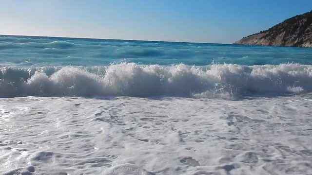 Transparent turquoise rough sea with comber and white foam and blue sky in a sunny day. Close up.