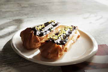 White plate with chocolate eclairs on wooden table. Top view.