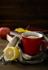 a cup of hot tea with lemon wrapped in a scarf on a wooden table with books in the background