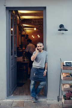 Young owner talking with cell phone at the entrance of the coffee shop