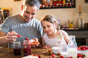 A dad preparing a slice of strawberry jam for his little girl