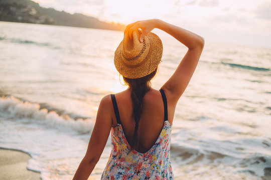 Young woman with hat watching sunset on the beach.