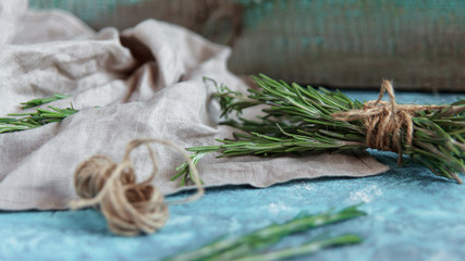 A bunch of fresh rosemary on linen cloth, Rustic greenery on blue wooden background.