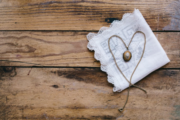 Vintage locket with chain laid out in the shape of a heart on lace handkerchief, with copyspace
