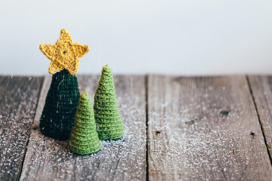Three little crocheted christmas trees with artificial snow on a rustic wooden table