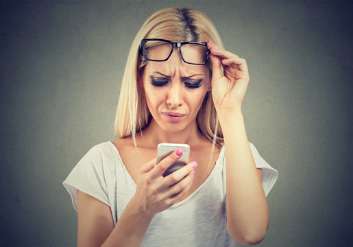 woman with glasses having trouble seeing cell phone has vision problems. Confusing technology