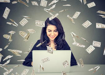 Happy woman using a laptop building online business under dollar bills falling down.