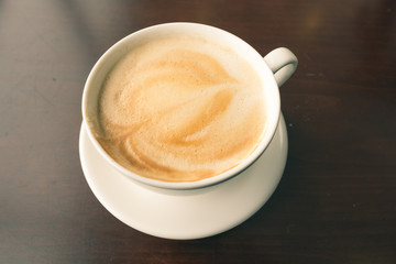 Hot cappuccino coffee served on wooden table with side light window from left side