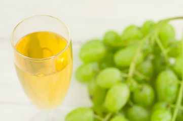 Transparent and fragile glass full of wine near bunch of fresh ripe green grapes on old wooden rustic white planks