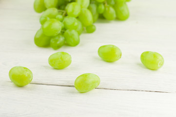 Scattered grapes beside bunch of fresh ripe green grapes on old wooden rustic white planks