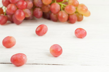 Scattered grapes beside bunch of fresh ripe rose grapes on old wooden rustic white planks