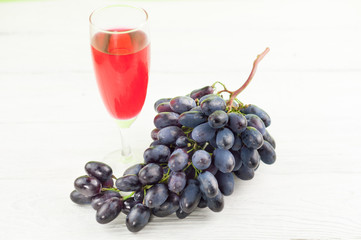 Bunch of fresh ripe blue grapes near transparent and fragile glass full of wine on old wooden...