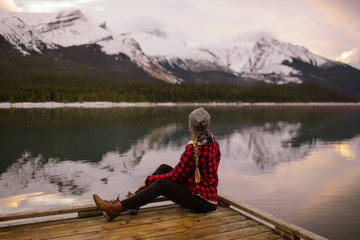 Woman with Long Hair Sitting On A Dock on a Mountain Lake on a Winter Morning